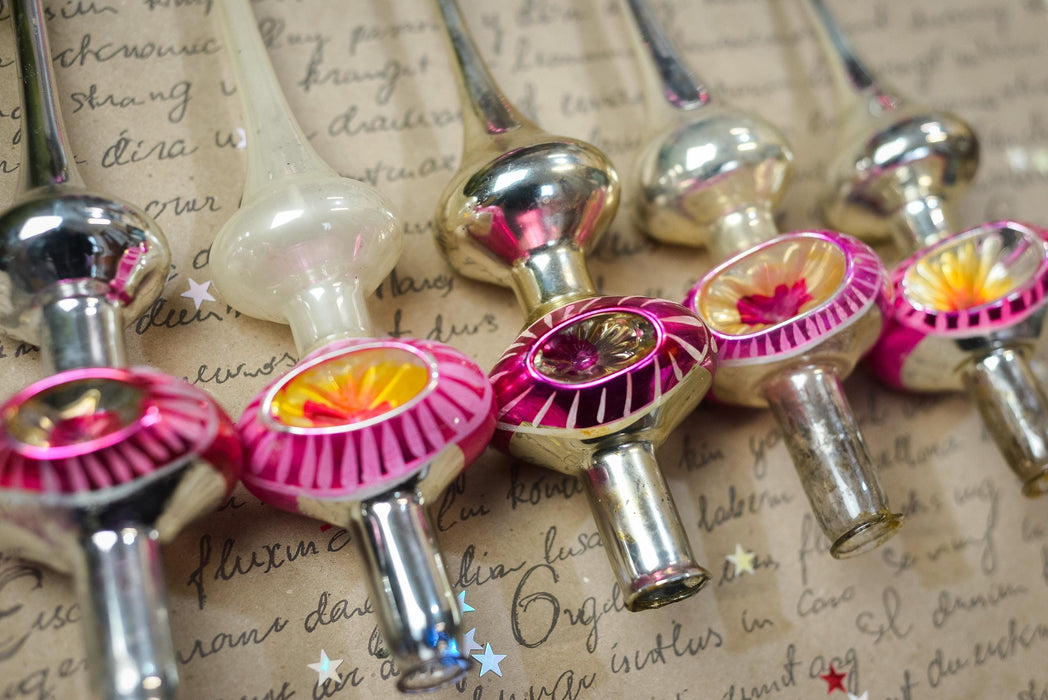 A collection of vintage Christmas ornaments, including glass and metal pieces with colorful designs, arranged on a surface with handwritten text.