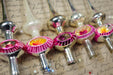 A collection of vintage Christmas ornaments, including glass and metal pieces with colorful designs, arranged on a surface with handwritten text.