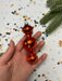 A hand holding a red glass ornament with a silver finial, surrounded by scattered confetti and a sprig of greenery.