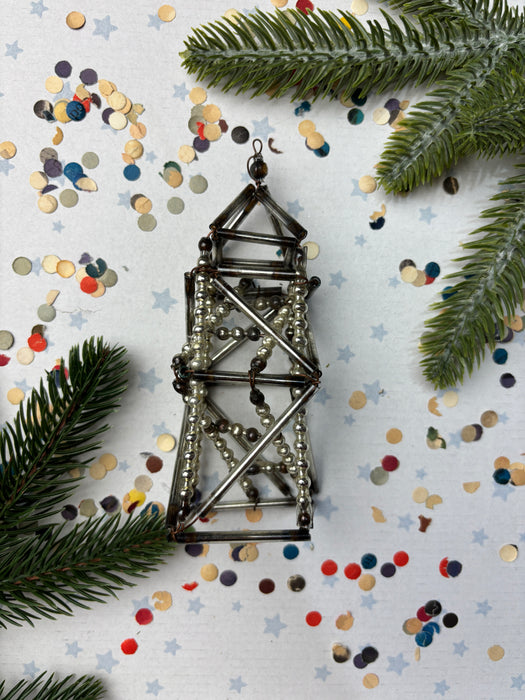a metallic structure with beads and a star-shaped ornament, surrounded by pine branches, confetti, and scattered beads on a white background.