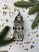 a metallic structure with beads and a star-shaped ornament, surrounded by pine branches, confetti, and scattered beads on a white background.