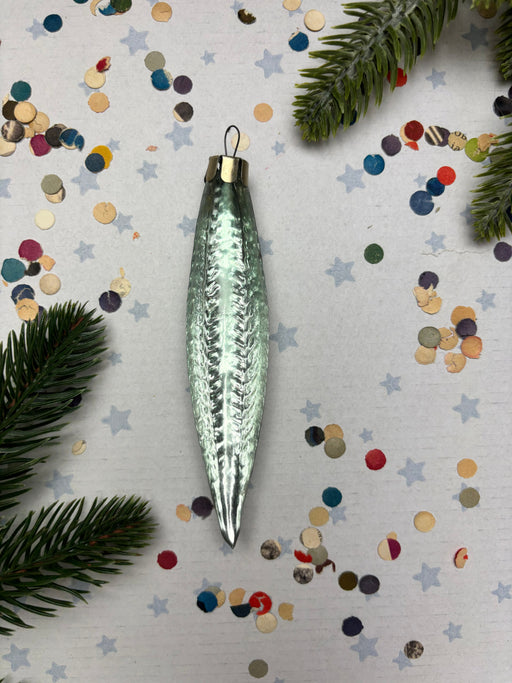A shiny, metallic ornament with a textured surface is placed on a background of colorful confetti and pine branches.