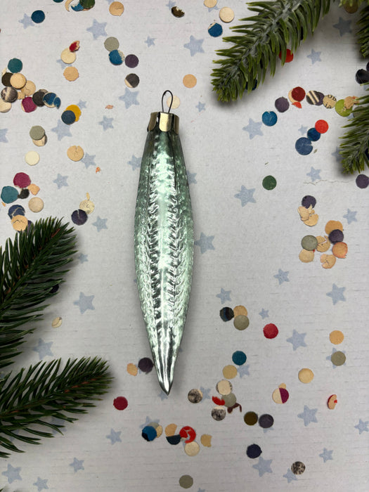 A shiny, metallic ornament with a textured surface is placed on a background of colorful confetti and pine branches.
