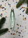 A shiny, metallic ornament with a textured surface is placed on a background of colorful confetti and pine branches.