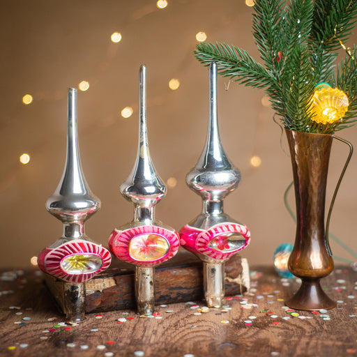 a festive scene with three vintage Christmas tree ornaments in the center, surrounded by a vase of greenery and twinkling lights.
