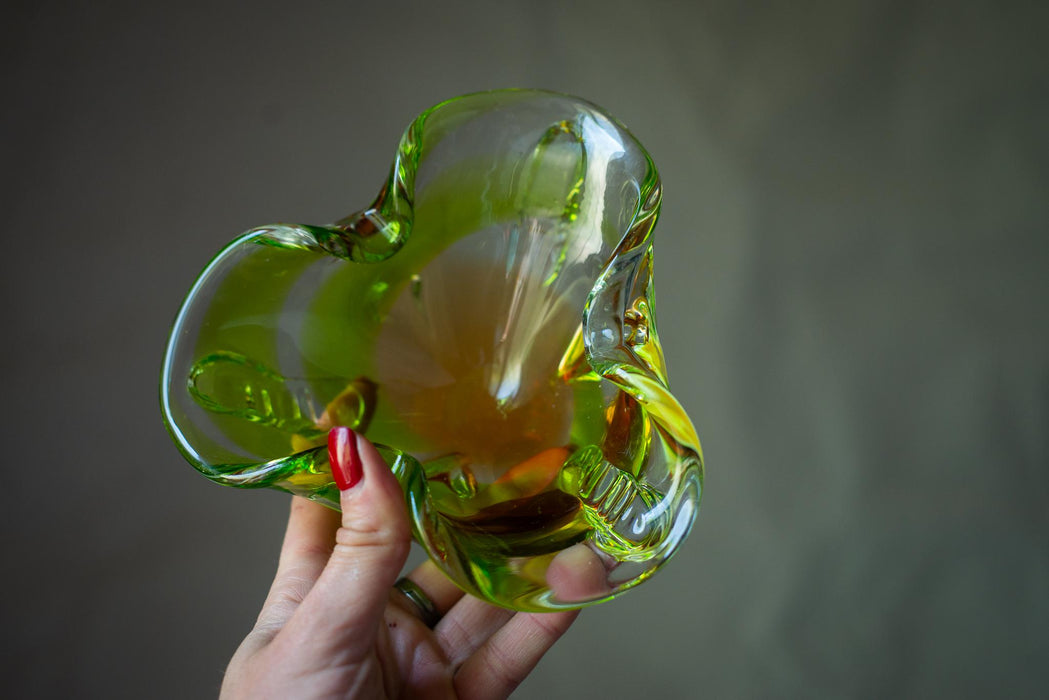 A hand holding a green glass sculpture with a yellowish tint.