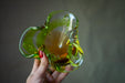 A hand holding a green glass sculpture with a yellowish tint.