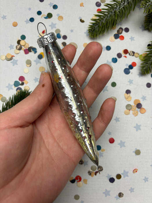 A hand holding a silver ornament with a pointed end, surrounded by colorful confetti on a white background.