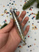 A hand holding a silver ornament with a pointed end, surrounded by colorful confetti on a white background.