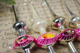 A close-up of several vintage Christmas ornaments, including a white ornament and a pink and purple ornament, resting on a surface with handwritten text.