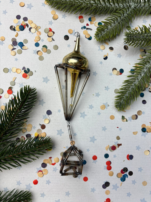 a Christmas ornament with a gold-colored finial, surrounded by confetti and pine branches.