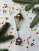 a Christmas ornament with a gold-colored finial, surrounded by confetti and pine branches.