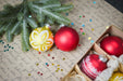 Christmas ornaments, including a yellow and white ornament and a red ornament, placed on a table with a sheet of paper with handwritten text and small star decorations.
