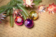 Christmas ornaments, including two purple and one gold, resting on a piece of paper with handwritten text.